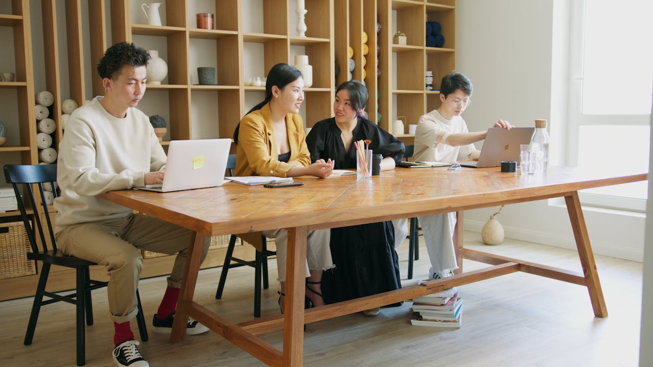 about-img Group of coworkers discussing ideas around a wooden table in a trendy office setting.